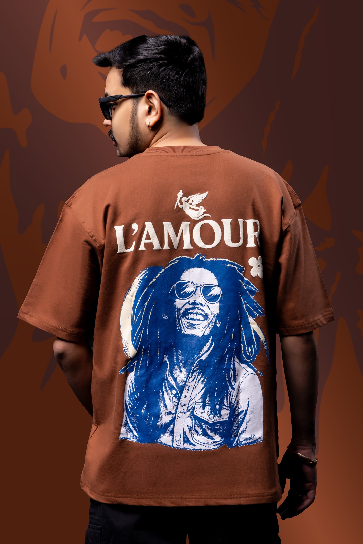 Person wearing a brown t-shirt with a graphic of a person with blue hair and 'L'AMOUR' text on the back against a brown background.