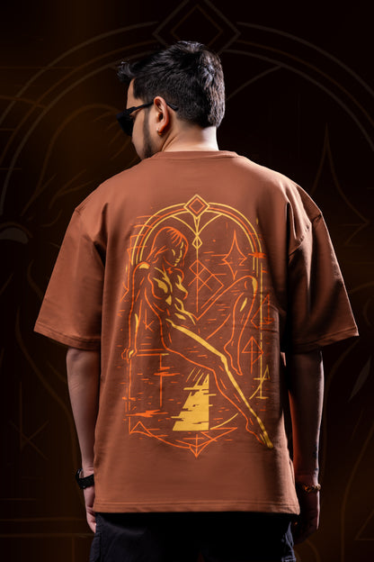 Person wearing a brown t-shirt with a geometric design on the back against a dark background